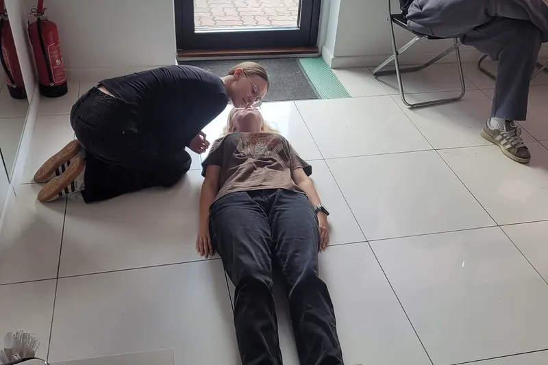 Kursantka pochyla się nad osobą leżącą na podłodze i sprawdza, czy oddycha