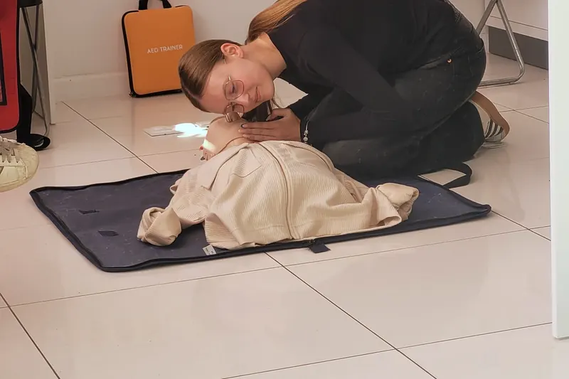 Kursantka wykonuje oddechy ratownicze na fantomie leżącym na macie